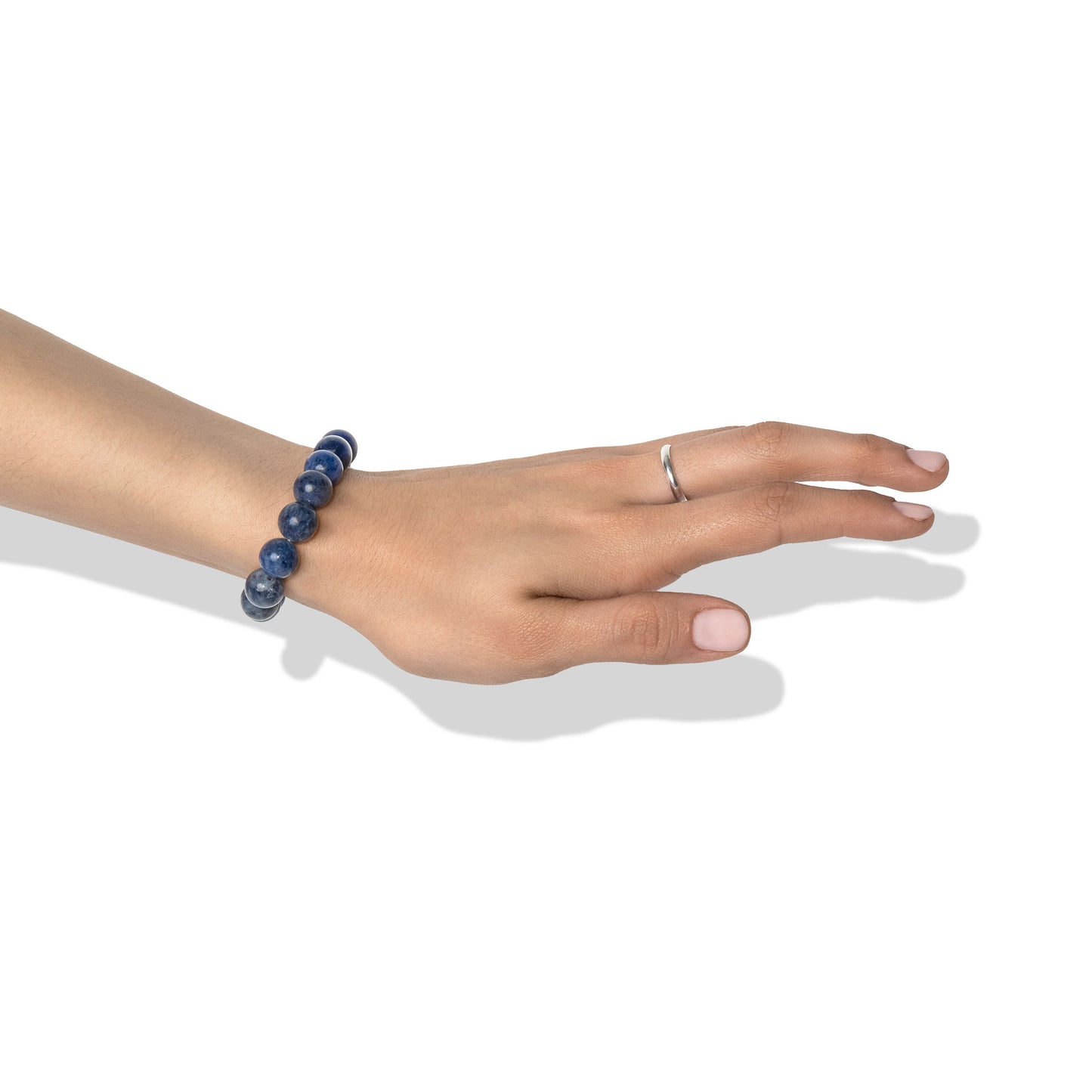 A single crystal gemstone bracelet made of sodalite, positioned on a hand adorned with a silver ring and light pink nail polish.