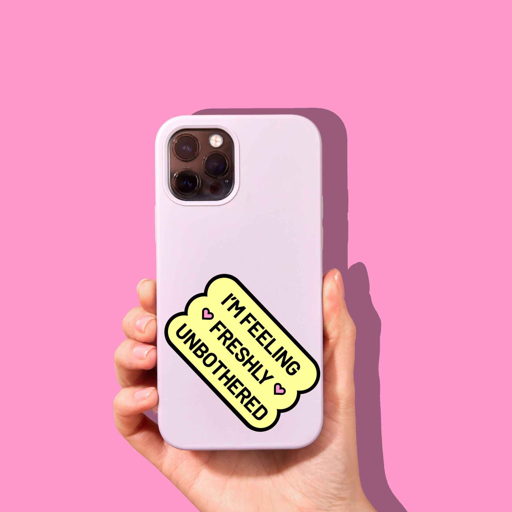 A woman holds up a cellphone with a pink case and a yellow sticker on it. The phone casts a shadow on a bright pink background.