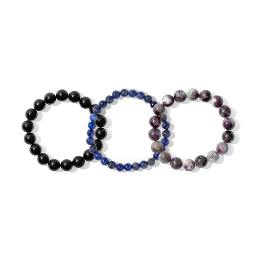 Three crystal gemstone bracelets on a white background. They are a mixture of purple, dark blue, and black colours.