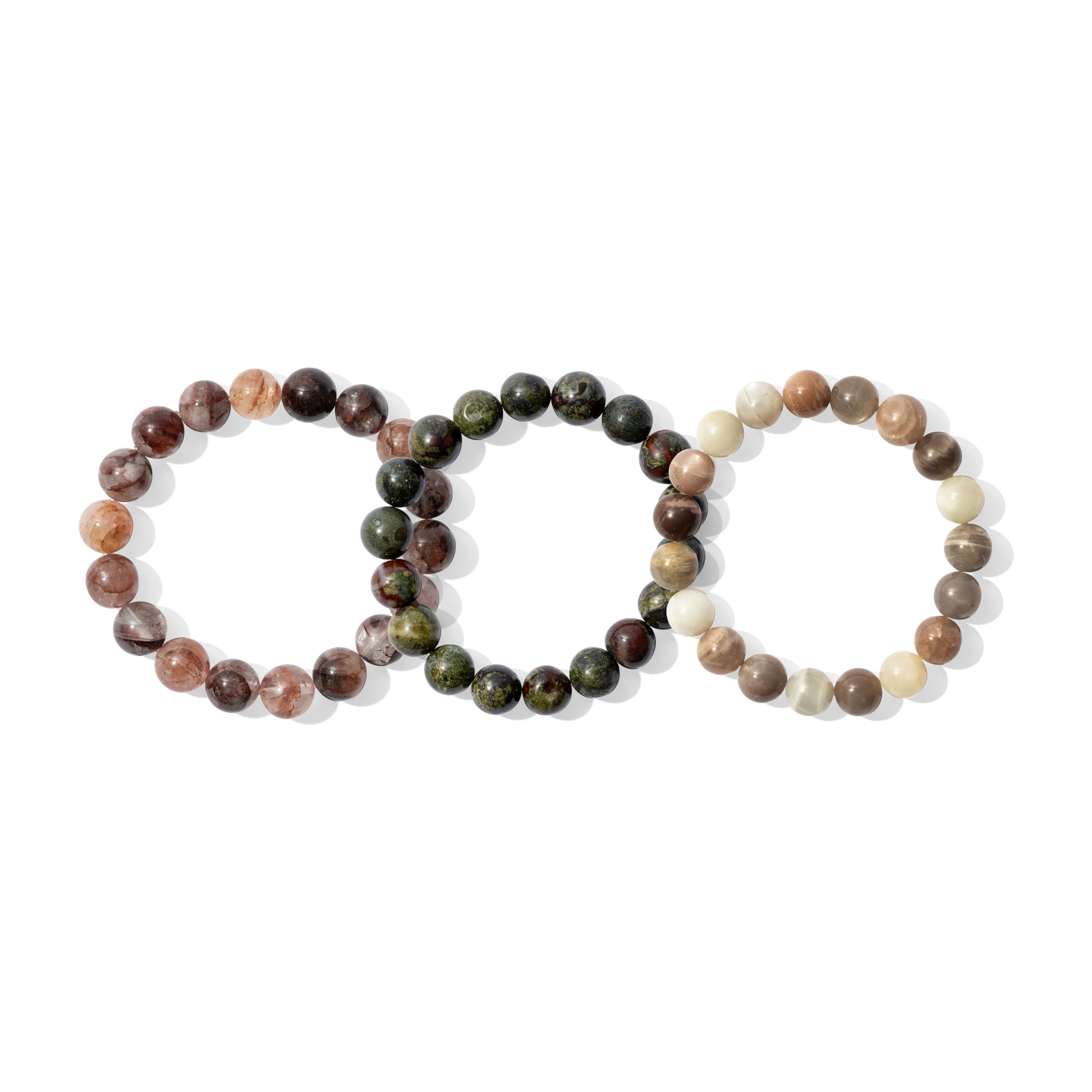 Three crystal gemstone bracelets on a white background. They are a mixture of red, deep green, cream, and earth toned colours.