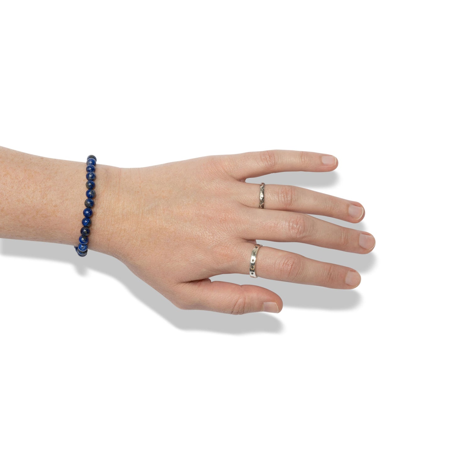 A single crystal gemstone bracelet made of lapis lazuli, positioned on a hand adorned with two silver rings.