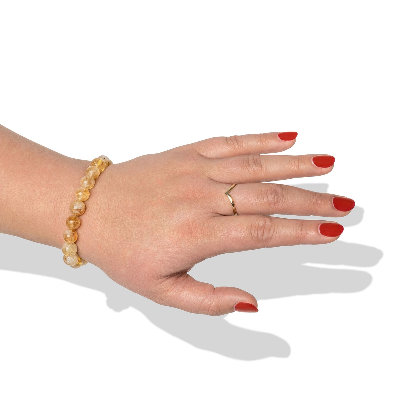 A single crystal gemstone bracelet made of citrine, positioned on a hand with one gold ring and bright red nail polish.